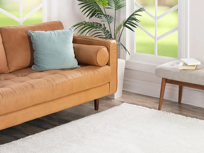 Tapis blanc recouvrant un sol en bois à côté d’un canapé et de fenêtres.